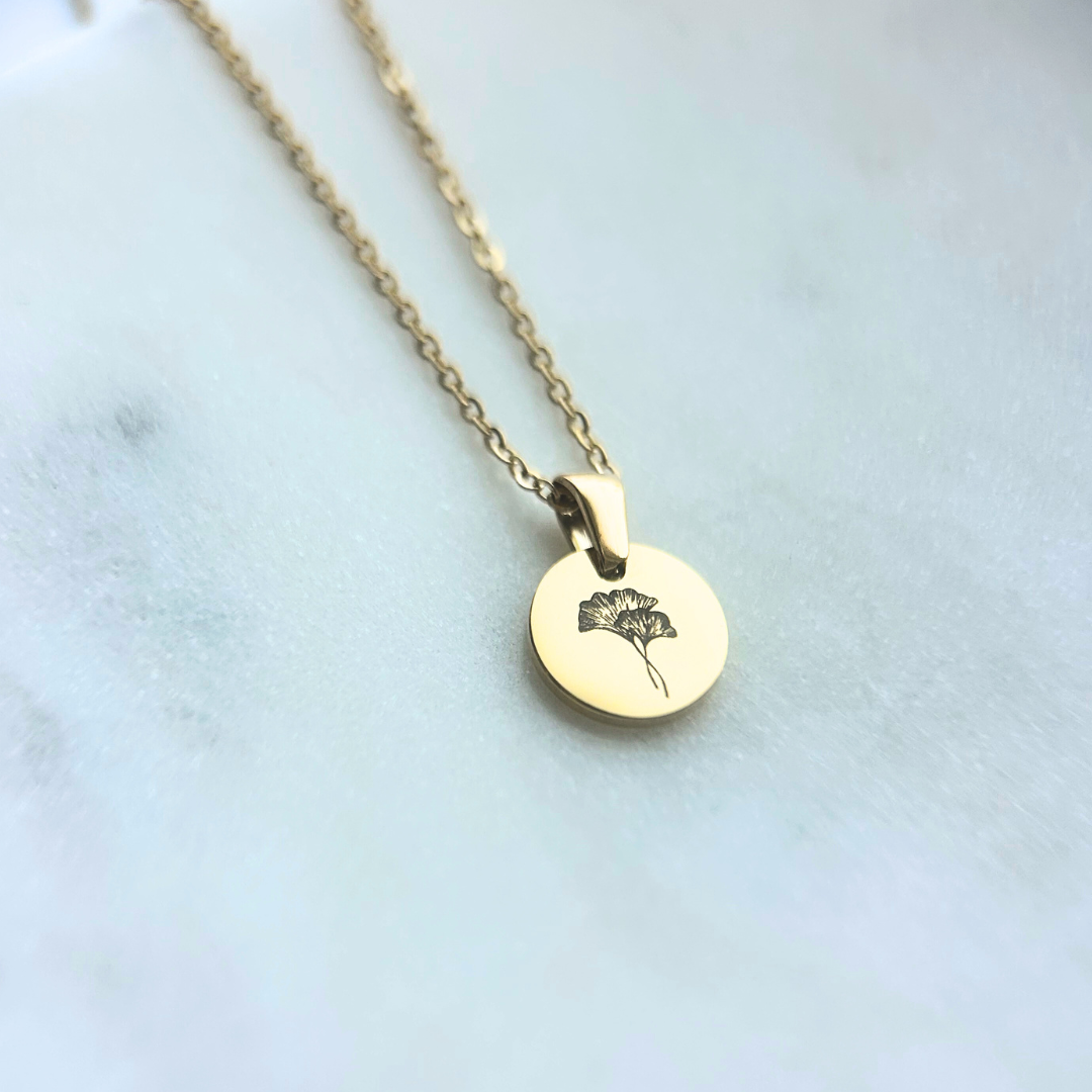 Gold necklace with a round pendant featuring a floral design on a light background