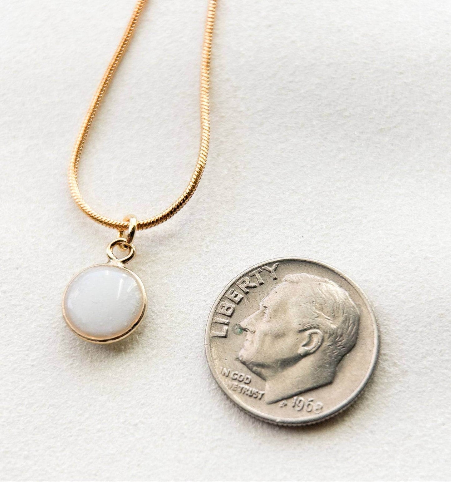 Breastmilk jewelry in a ball with gold chain, next to a dime.