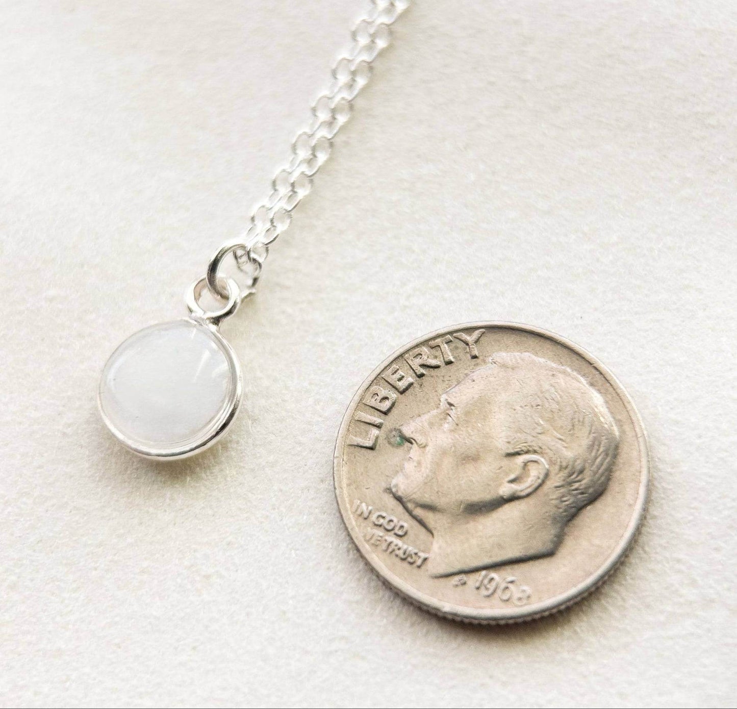 Breastmilk jewelry in a ball with silver chain next to a dime.