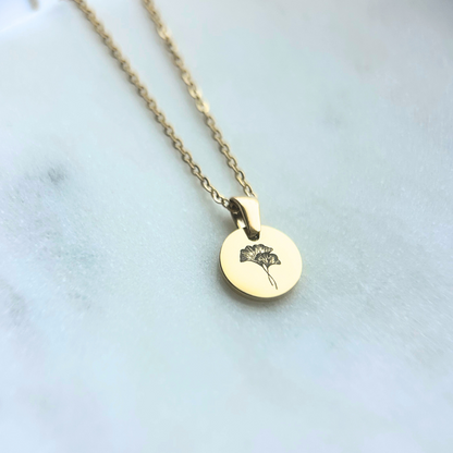 Gold necklace with a round pendant featuring a floral design on a light background