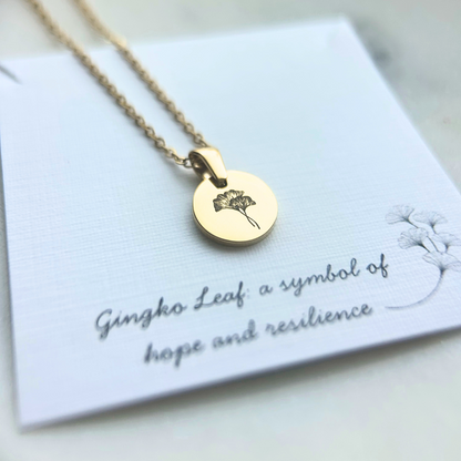 Gold necklace with a round pendant on a card with text about the symbol of the Gingko Leaf.