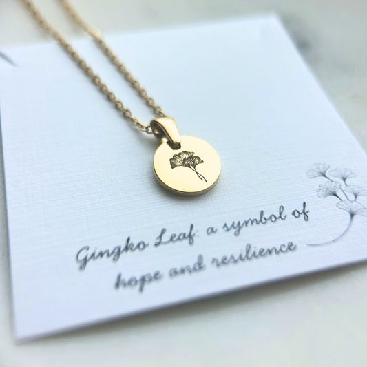 Gold necklace with a round pendant on a card with text about the symbol of the Gingko Leaf.