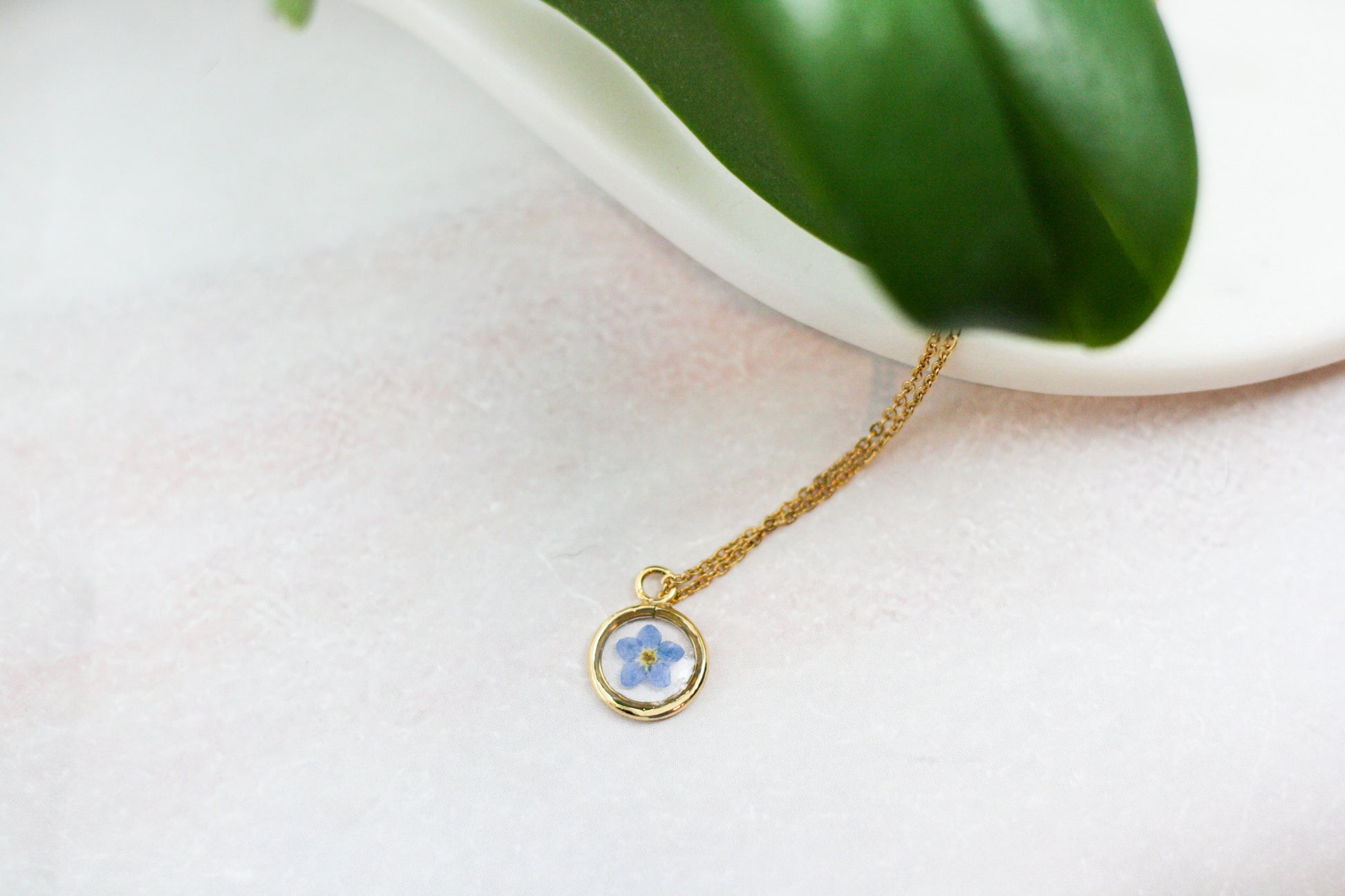  gold forget me not necklace with a green leaf in the foreground