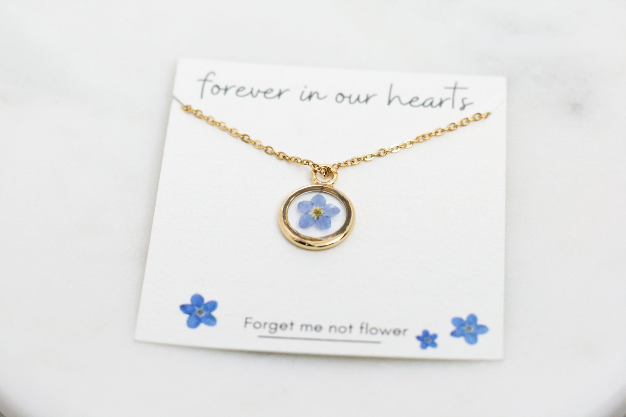 gold forget me not necklace in a gold pendant on a card reading 