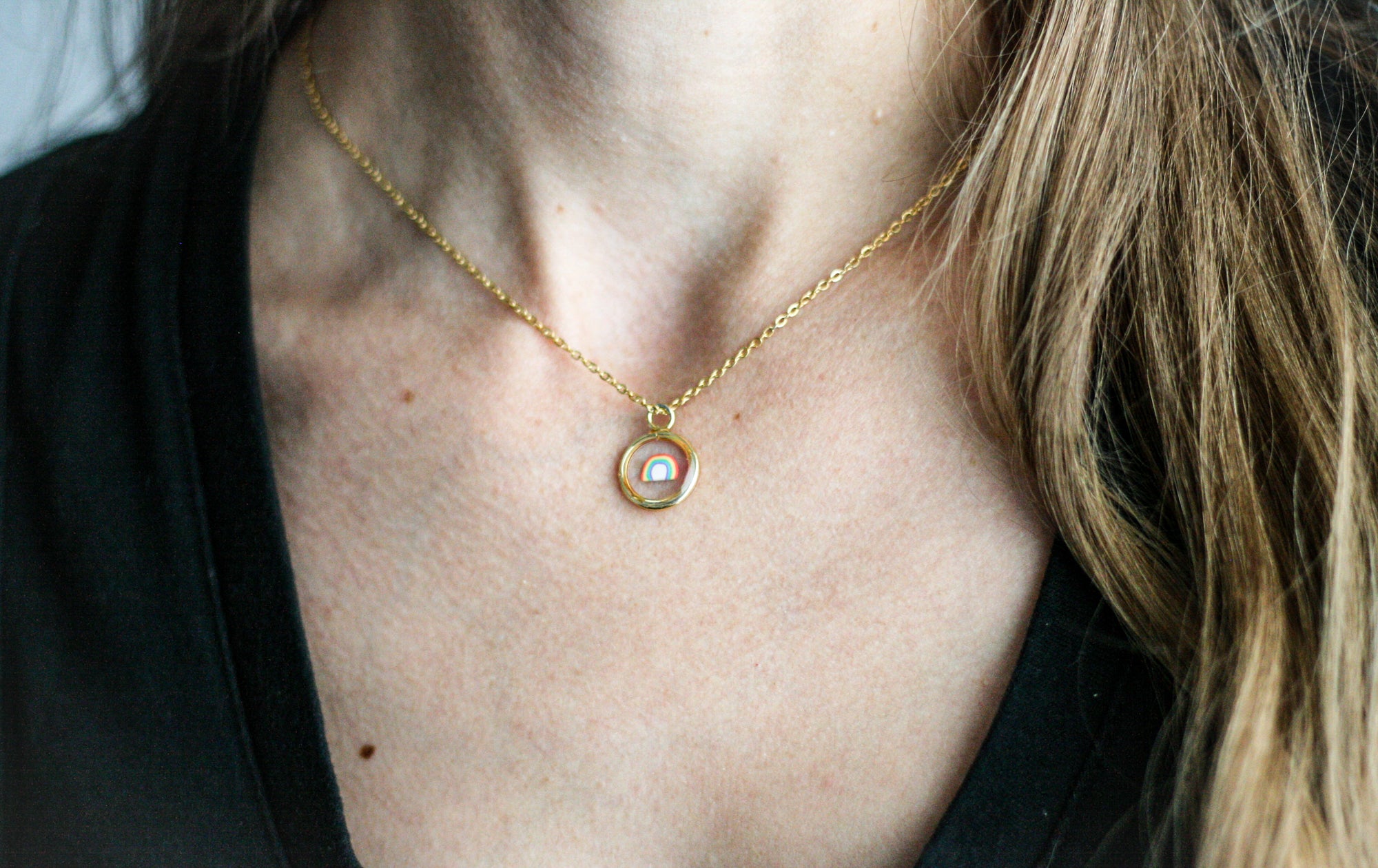 woman wearing a gold necklace with a clay rainbow inside 