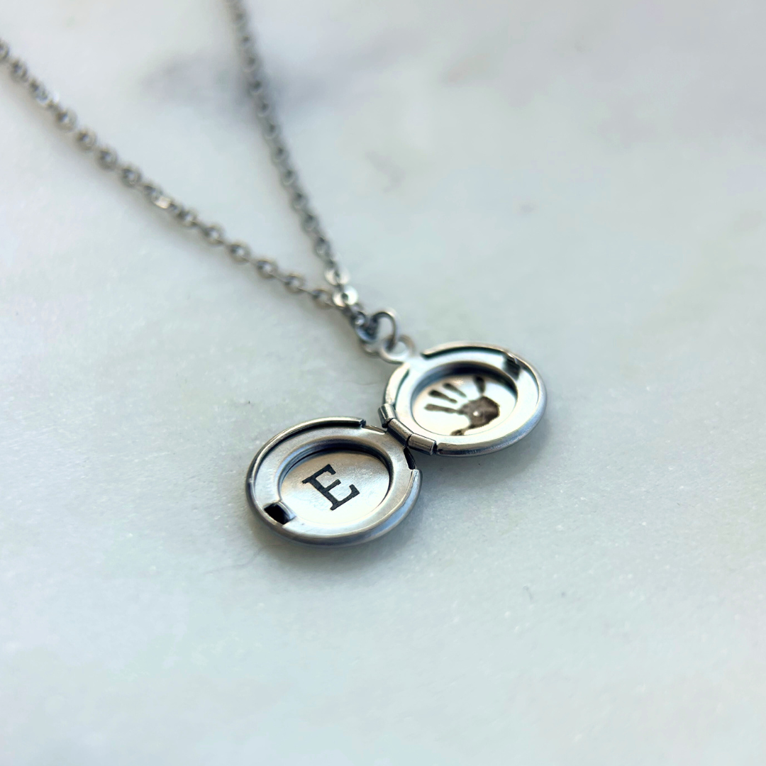 Rest of the Nest silver necklace with a locket featuring an engraved letter 'E' on a light background