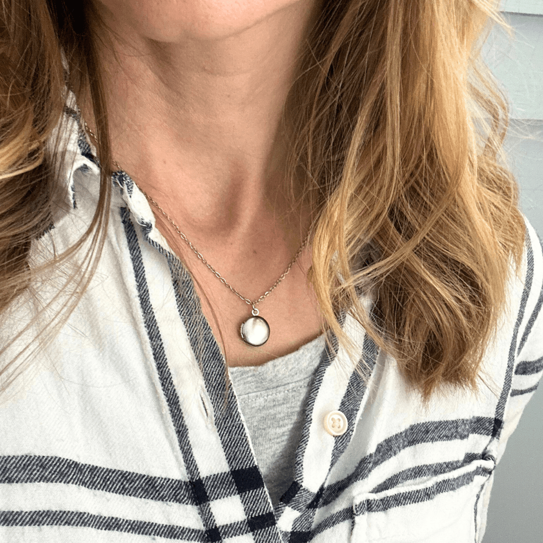 Rest of the Nest mini handprint locket Close-up of a person wearing a necklace with a pendant, with a blurred background.