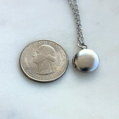 Rest of the Nest Silver locket on a chain next to a U.S. quarter dollar coin for a size comparison on a white background