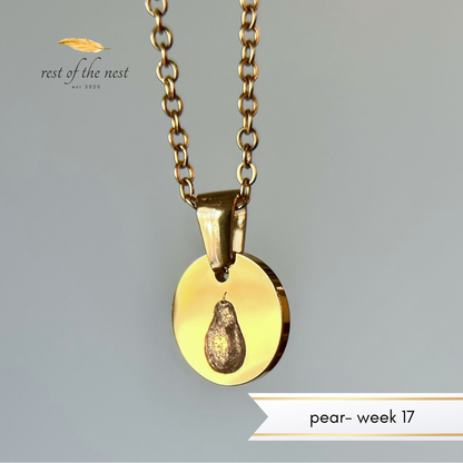 Rest of the Nest Gold necklace with a pear engraved on pendant on a gray background.