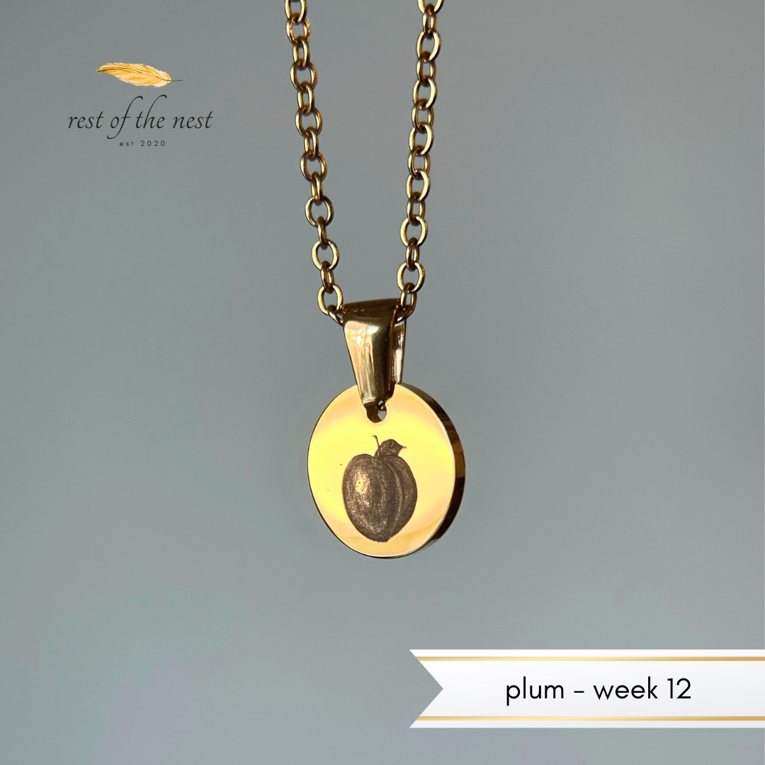 Gold necklace with a plum engraved on a pendant on a gray background.