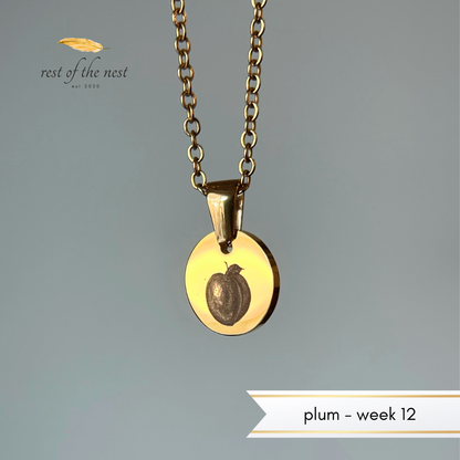 Gold necklace with a plum engraved on a pendant on a gray background.