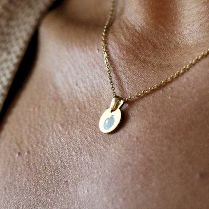 Rest of the Nest Gold necklace with a peach engraved on a pendant on a person's neck