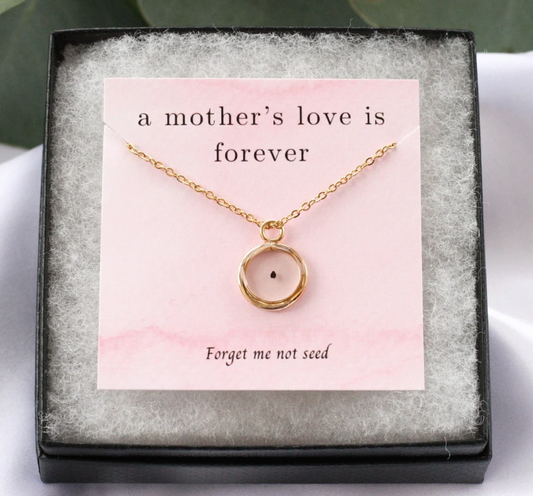 gold pendant necklace with forget me not seed inside on a card reading "a mothers love is forever" and "forget me not seed" at the bottom