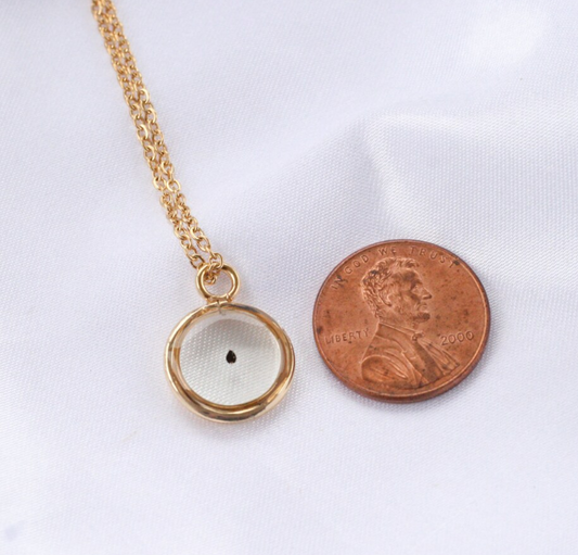 gold forget me not seed necklace next to a penny for size comparison