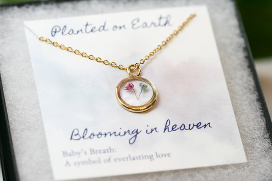 a piece of pink and blue babys breath in a gold pendant necklace