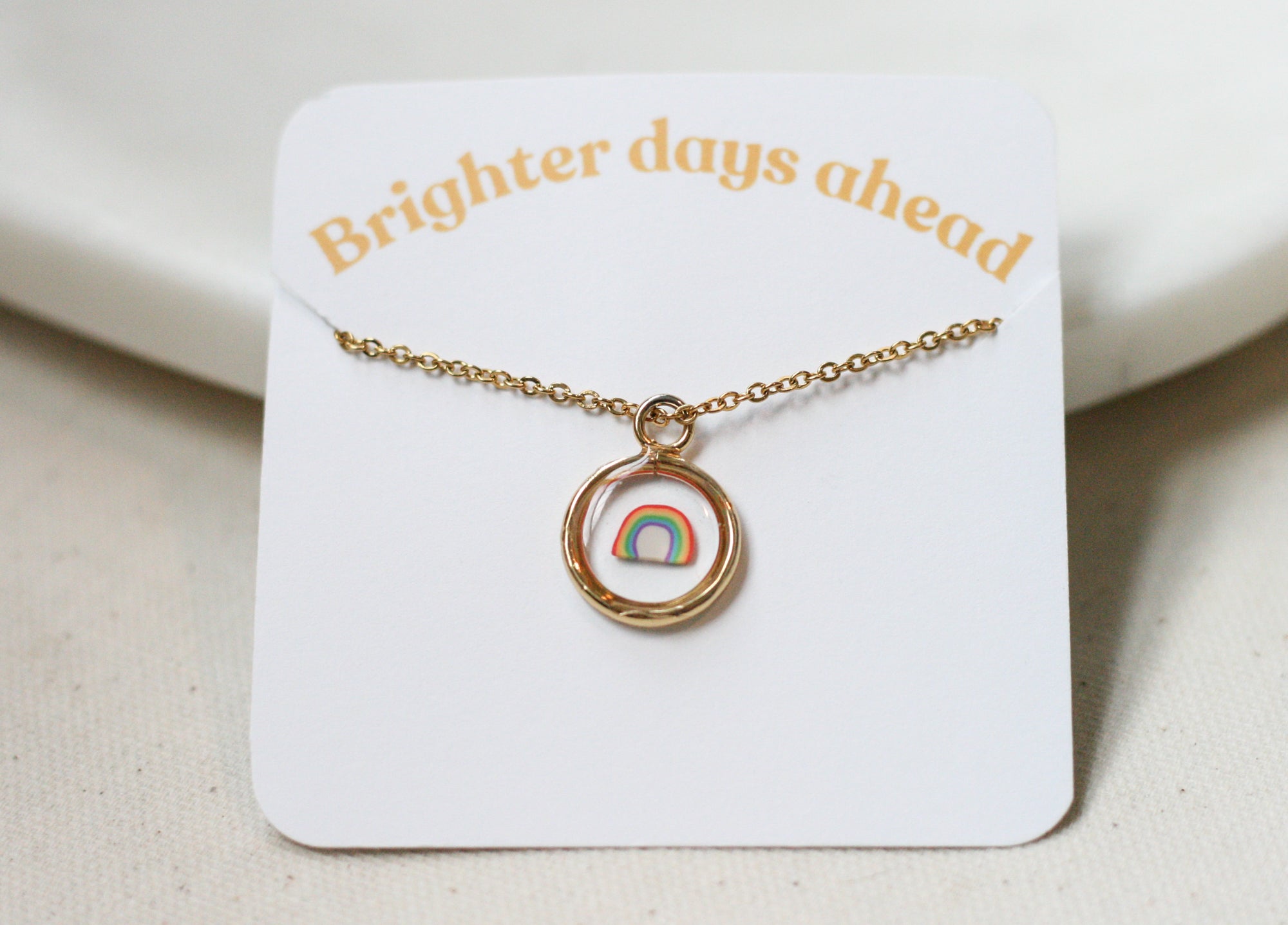 gold pendant necklace with a clay rainbow inside clear resin on a card reading 