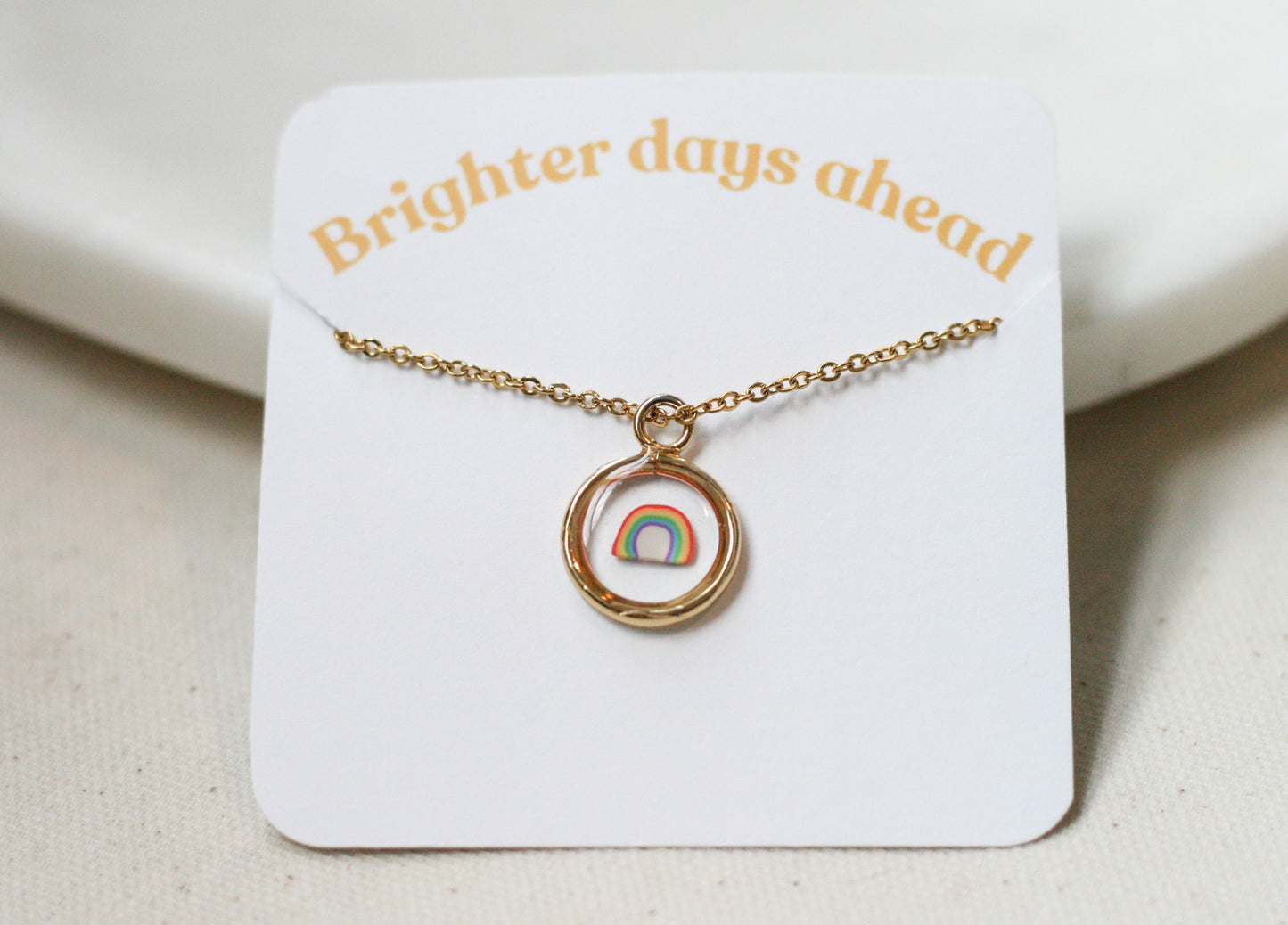 gold pendant necklace with a clay rainbow inside clear resin on a card reading "brighter days ahead"