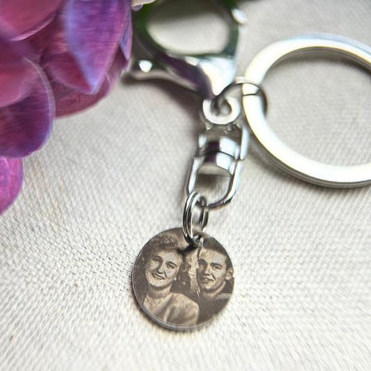 A Rest of the Nest keychain with a circular charm featuring a couple's engraved photo on a light fabric background.