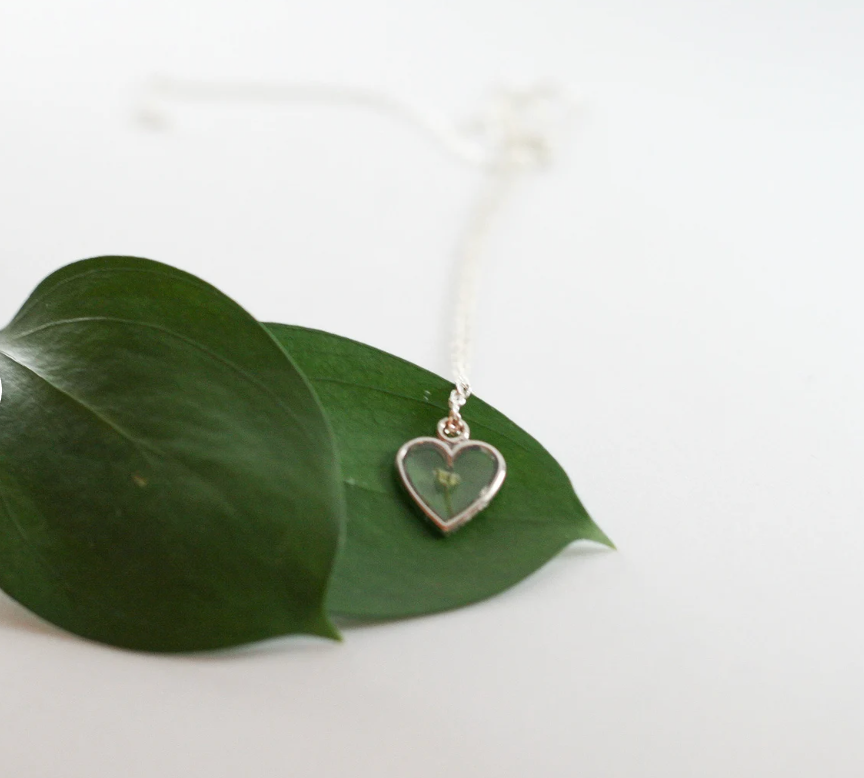 one piece of babys breath in a silver heart pendant resting on a green leaf