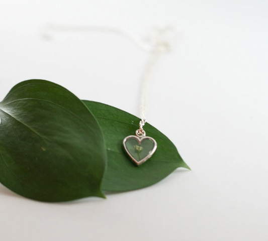 one piece of babys breath in a silver heart pendant resting on a green leaf