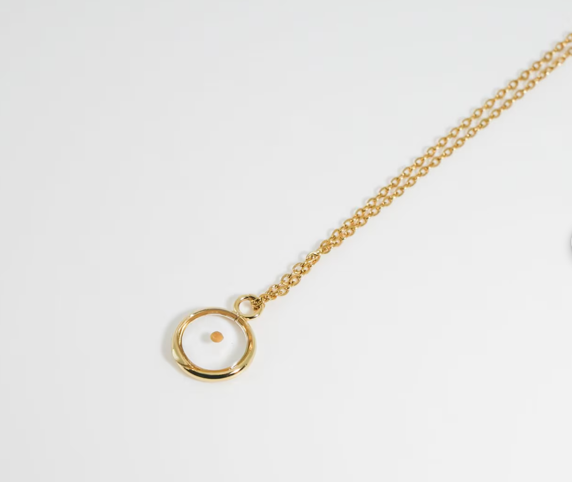 gold mustard seed necklace against a white background 