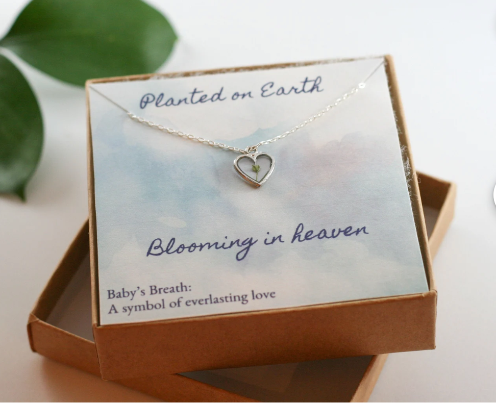 heart necklace with a piece of babys breath inside in a craft paper necklace box