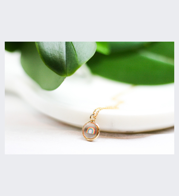 small clay rainbow inside of gold necklace with plants in the background 