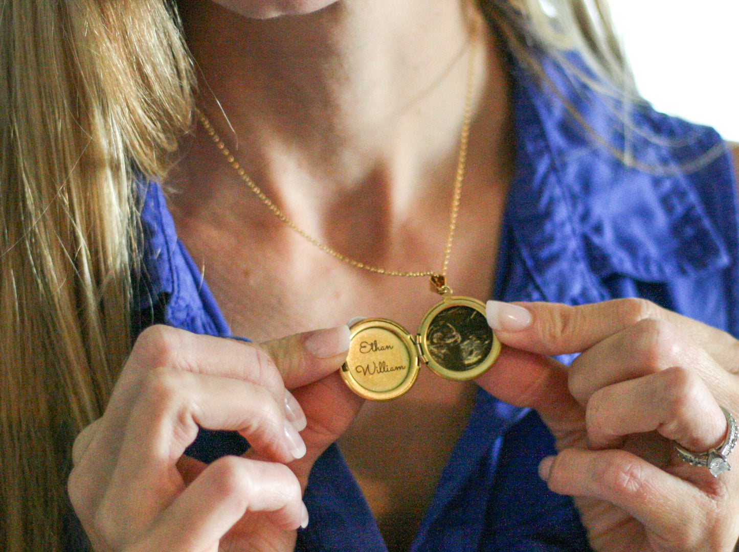 woman wearing a gold locket holding it open displaying an engraved sonogram and baby name